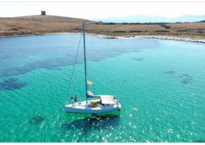 Asinara escursioni - barca ormeggiata nelle acque cristalline con l'Asinara nello sfondo. Prenotazione escursioni con Asinara Sail Experience.